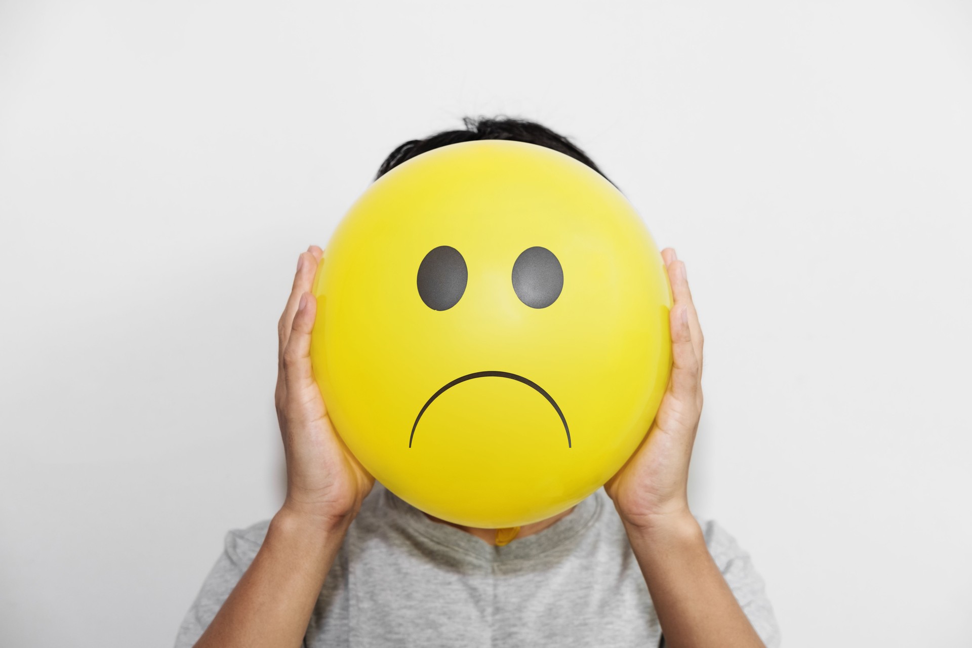 man holding a yellow balloon with sadly face emoticon